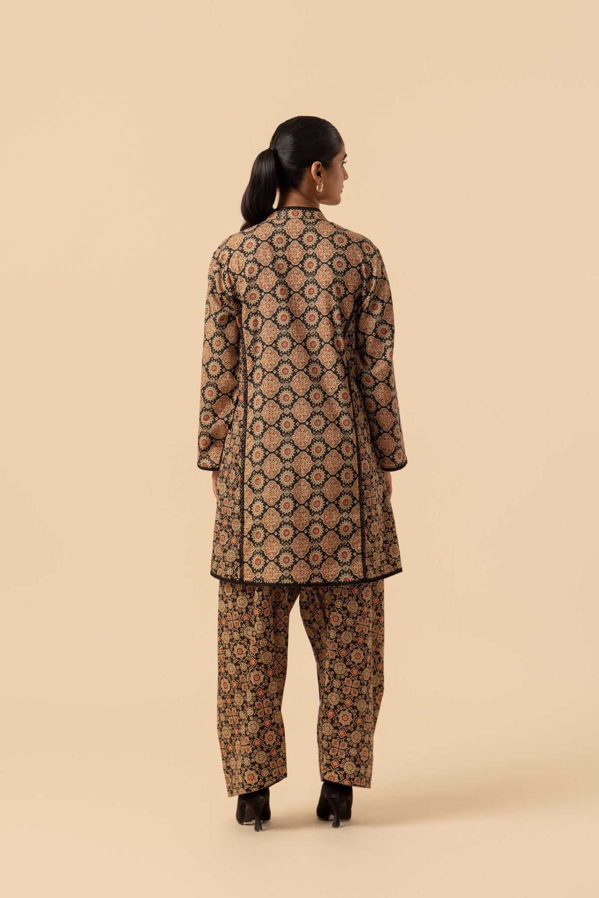 A woman viewed from the back wearing a matching ajrakh printed co-ord set. The fabric has an intricate geometric pattern in dark brown, black, and beige.