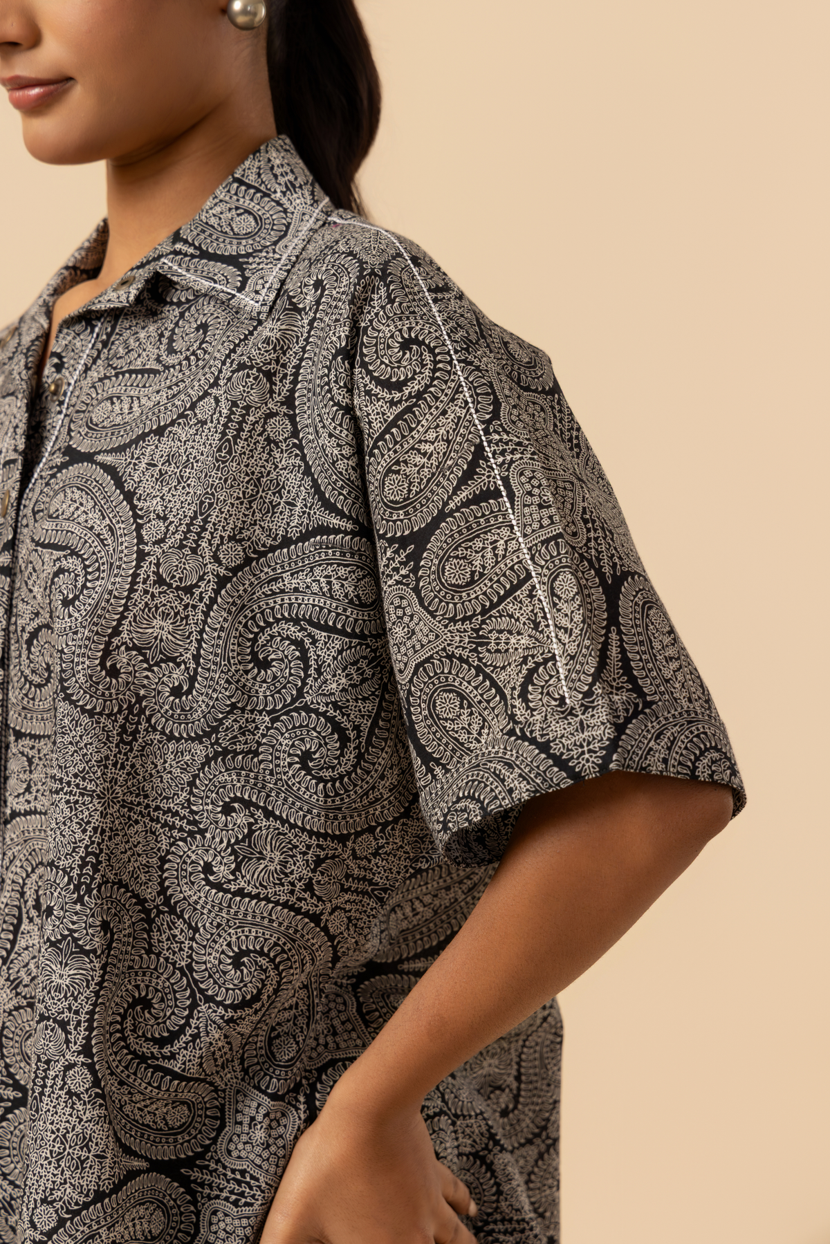 A model stands confidently in a matching patterned outfit, featuring a loose shirt stands against a soft beige background, showcasing a relaxed style.