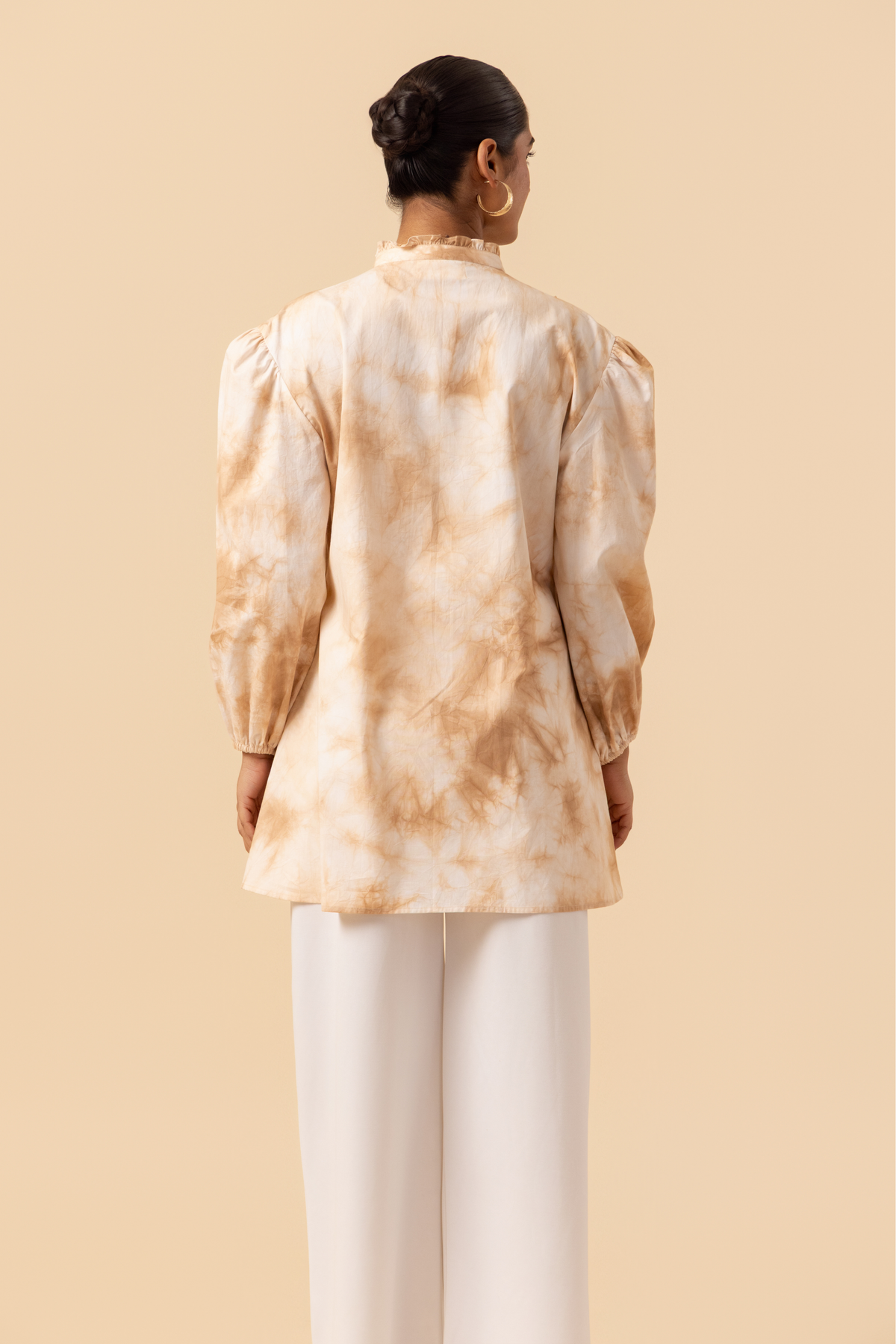 Back view of a woman wears a vibrant caramel tie-dye shirt dress with puffed sleeves, paired with white wide-leg trousers and stylish sandals.