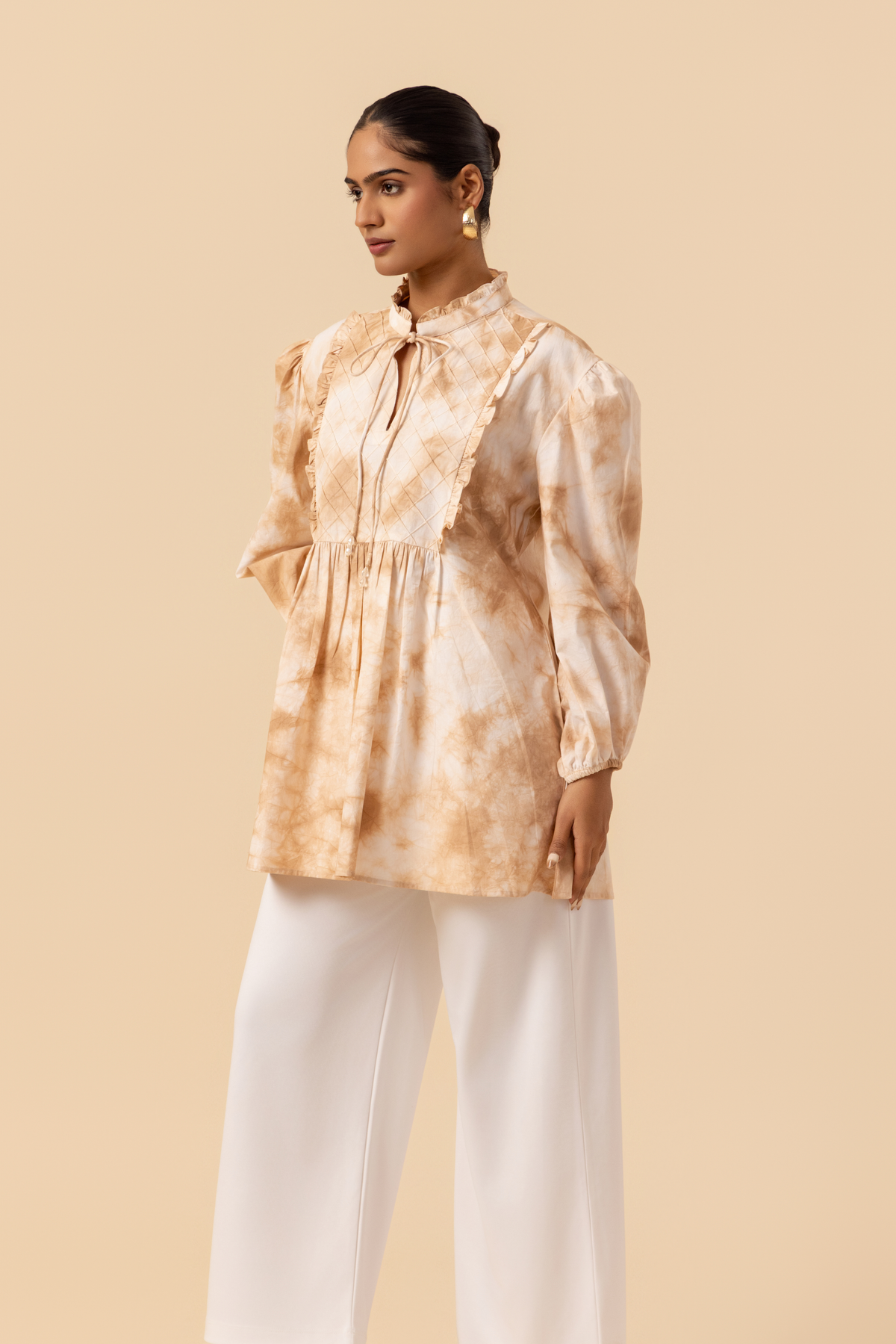 Side view of a woman wears a vibrant caramel tie-dye shirt dress with puffed sleeves, paired with white wide-leg trousers and stylish sandals.
