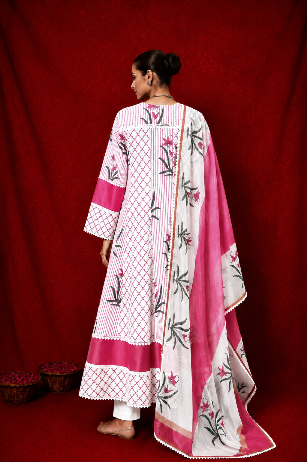 A woman shown from the back wearing a pink and white handblock printed anarkali suit with a matching draped scarf, set against a solid red backdrop.