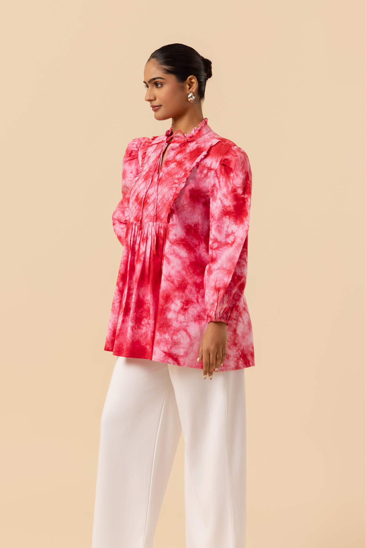 Side view of a model wears a vibrant cherry red tie-dye shirt dress with puffed sleeves, paired with white wide-leg trousers and stylish sandals.