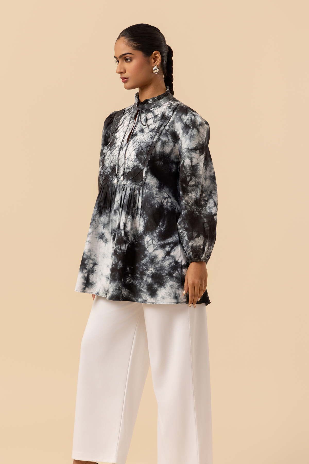 Side view of a model wears a vibrant black & white tie-dye shirt dress with puffed sleeves, paired with white wide-leg trousers and stylish sandals.