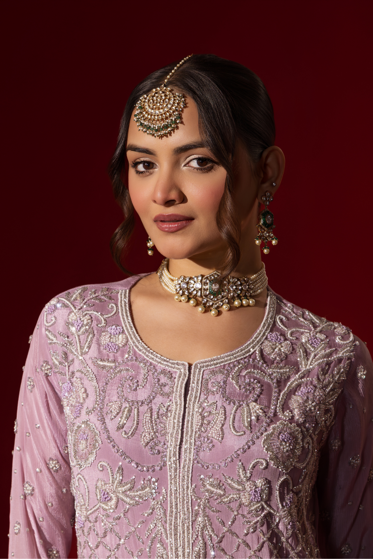 Closeup view of a woman stands confidently in a beautifully lavender embroidered kurta set, against a rich red background.