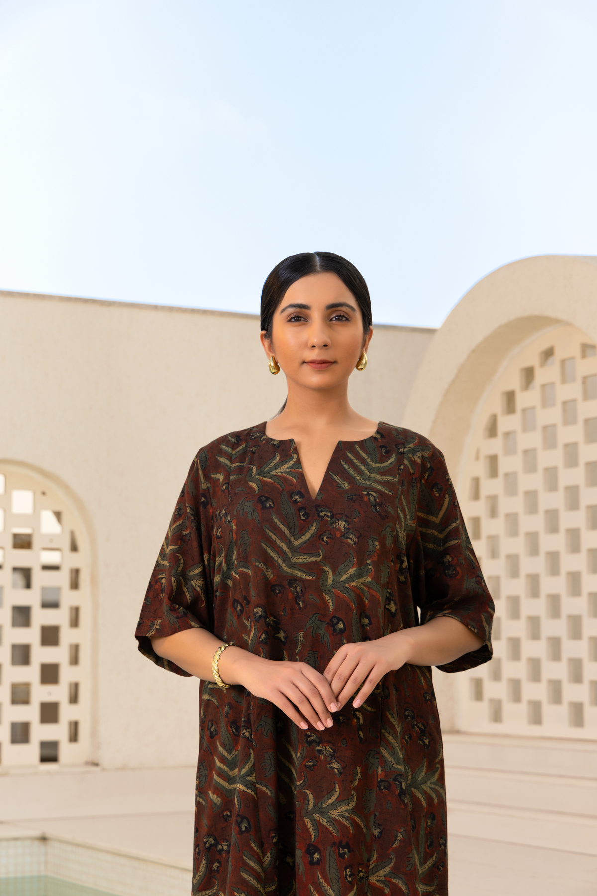 Closeup View of a Model wearing a brown printed kurta set with intricate patterns, paired with striped trousers, styled in a serene outdoor setting