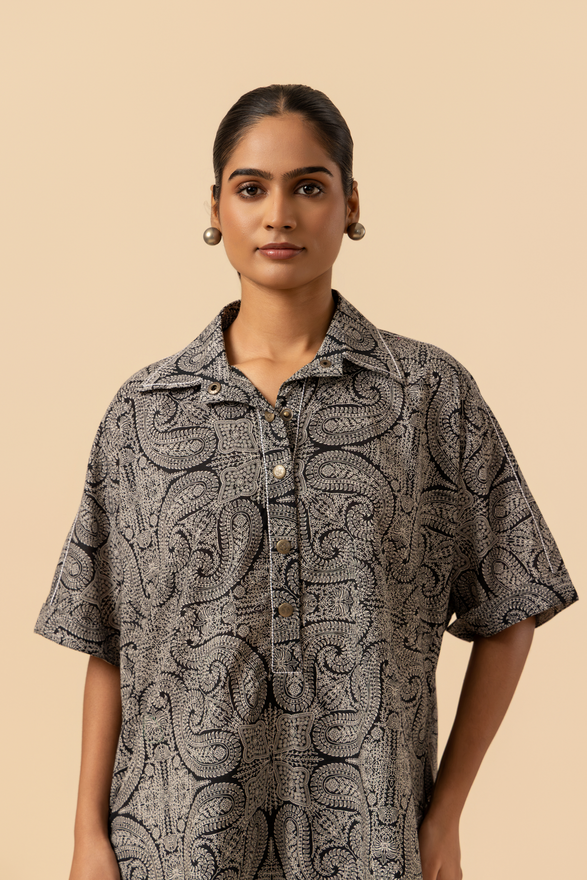 Closeup view of a person stands confidently in a matching patterned outfit, featuring a loose shirt and tailored pants, paired with stylish heels.