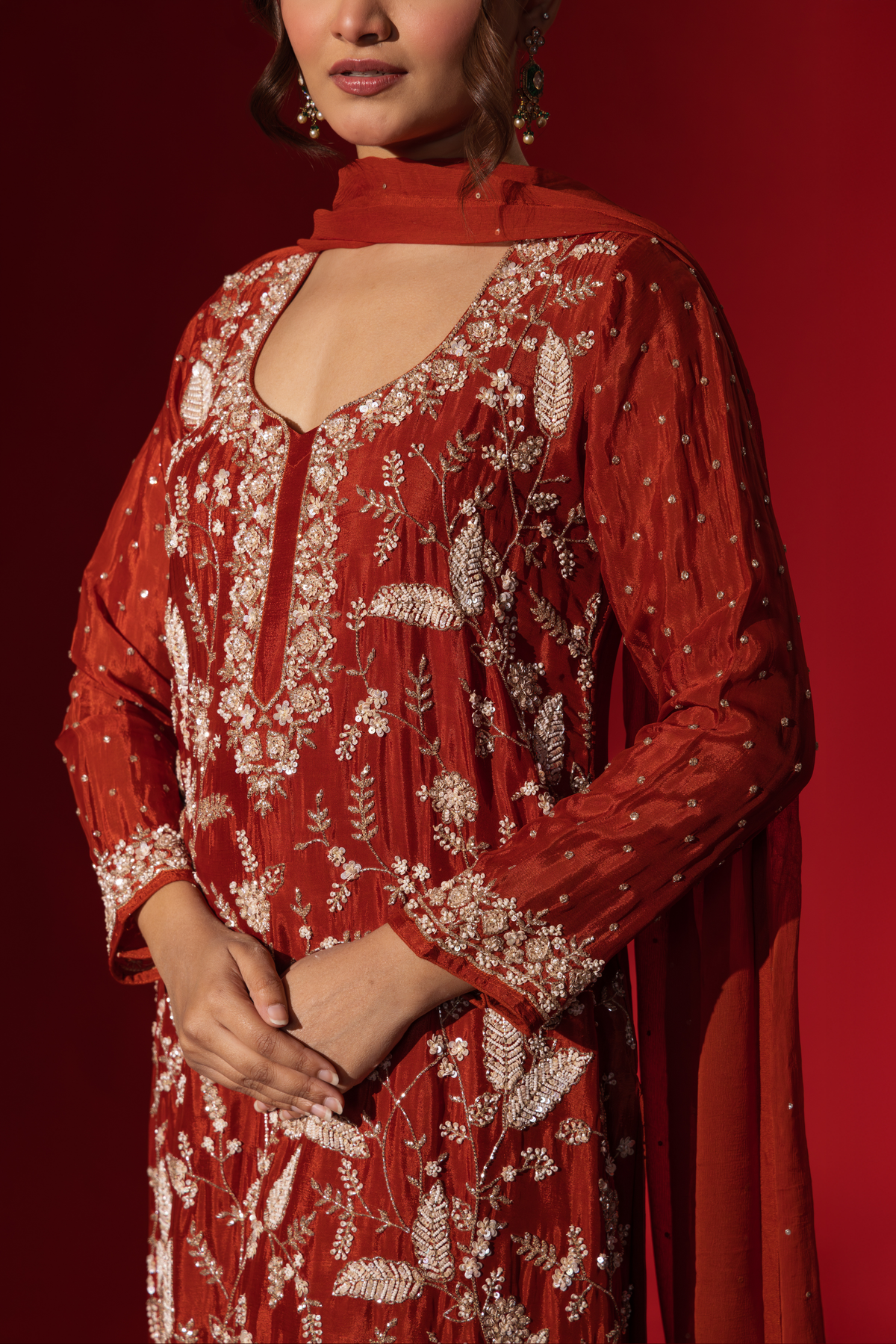 Closeup view of a woman's hand in an elegant red embroidered kurta set adorned with intricate white embroidery against a rich red background.