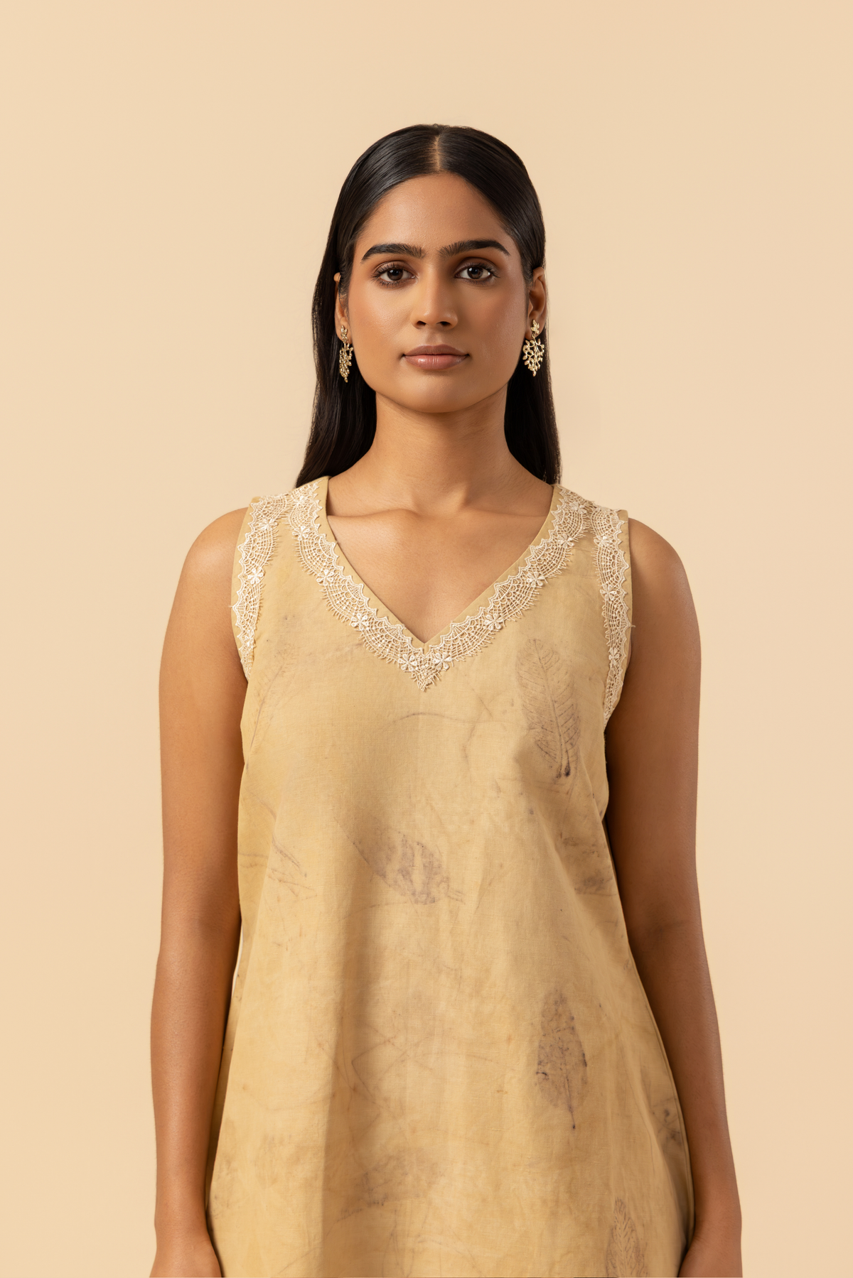 Front view of a person stands in a light beige outfit featuring a sleeveless top and matching pants, complemented by delicate lace detailing