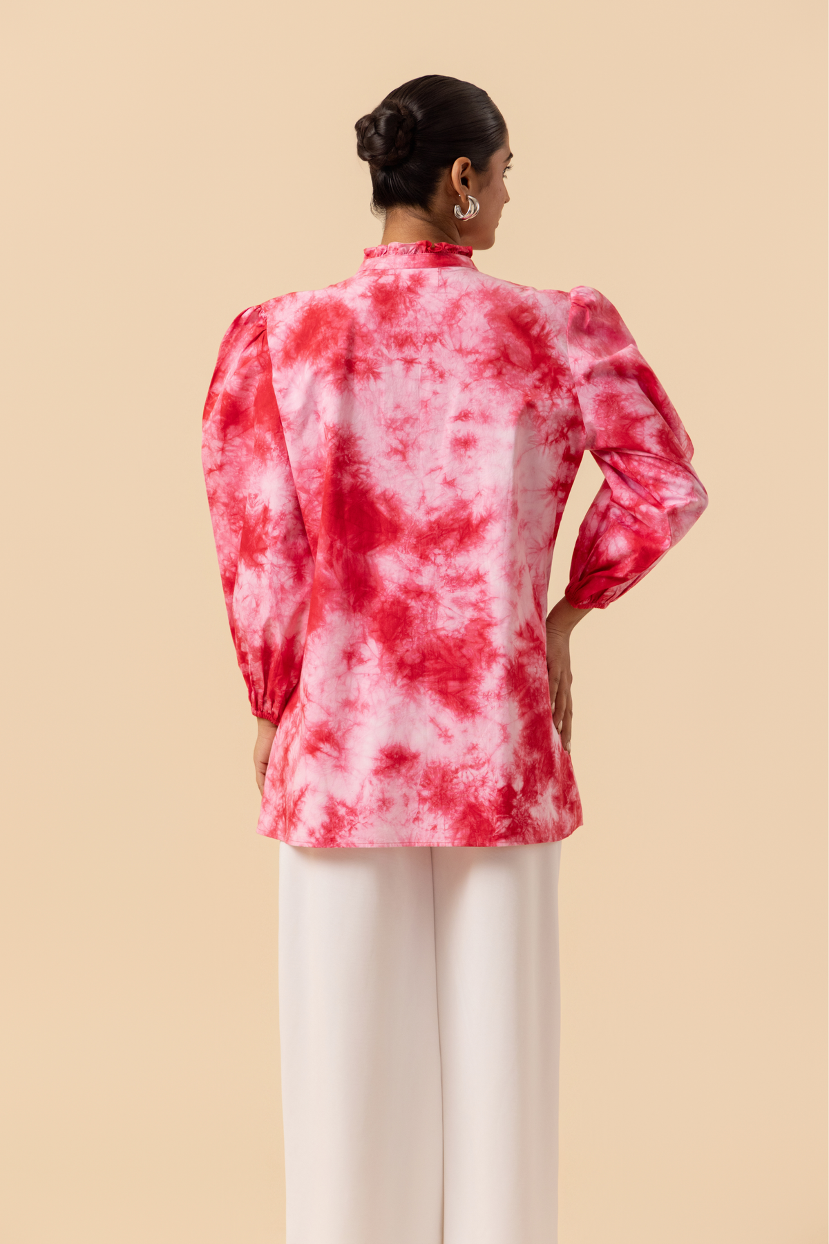 Back side view of a model wears a vibrant cherry red tie-dye shirt dress with puffed sleeves, paired with white wide-leg trousers and stylish sandals.