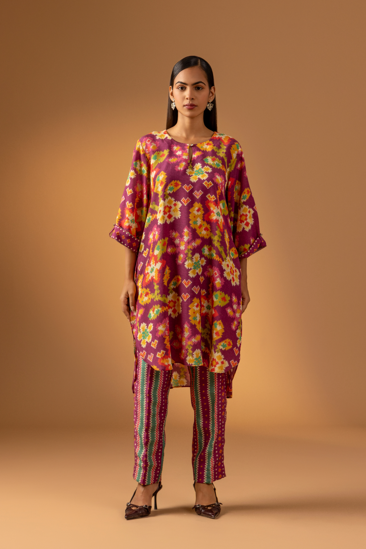 A model showcases a magenta floral-patterned co-ord set paired with colorful striped pants against a warm, neutral background.