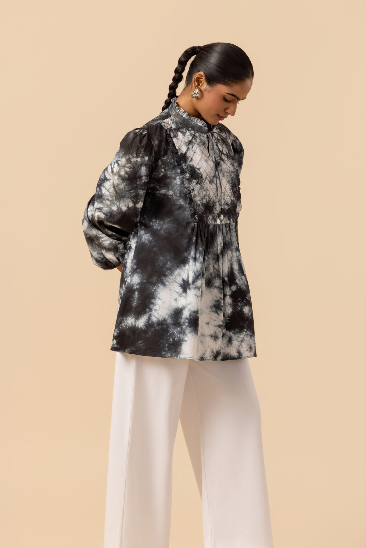 Right side view of a model wears a vibrant black & white tie-dye shirt dress with puffed sleeves, paired with white wide-leg trousers and stylish sandals.
