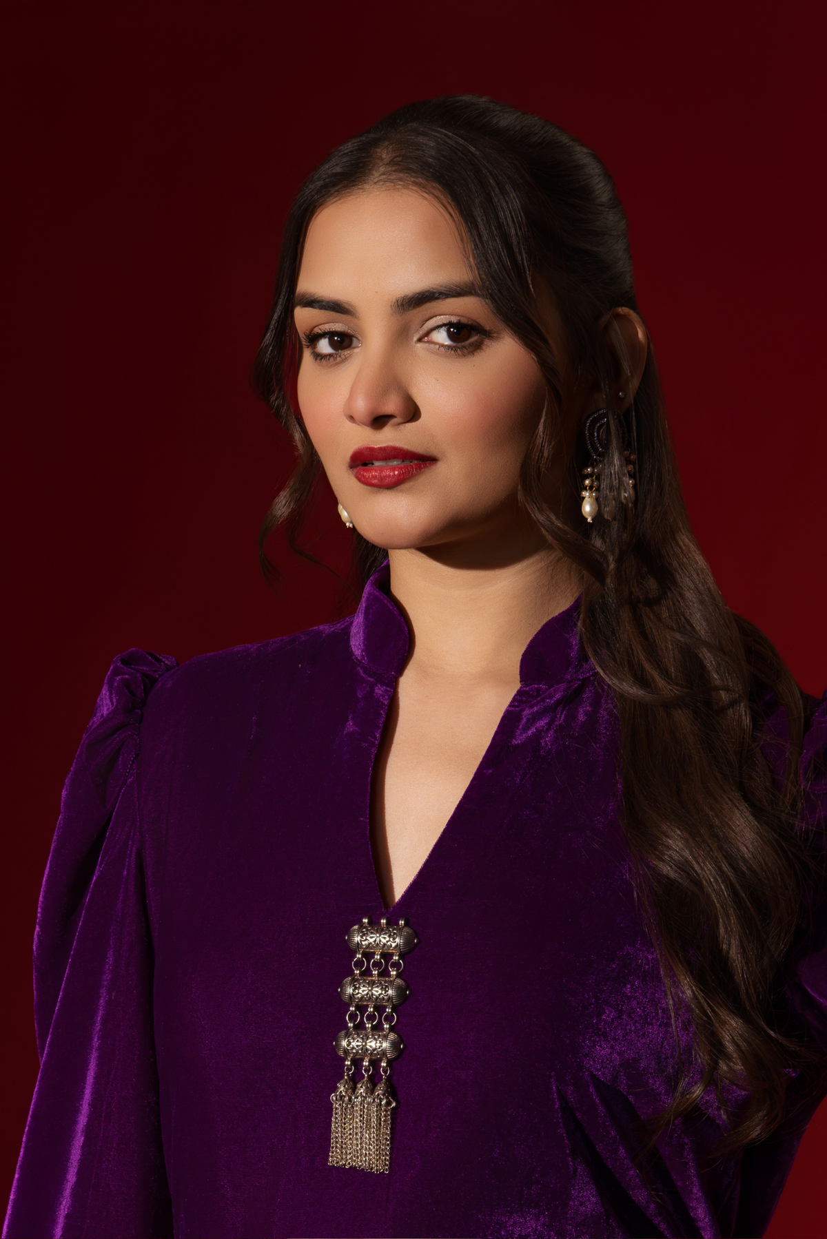 Closeup view of a woman in a vibrant purple velvet co-ord set with a feminine silhouette and elegant earrings, set against a rich red background.