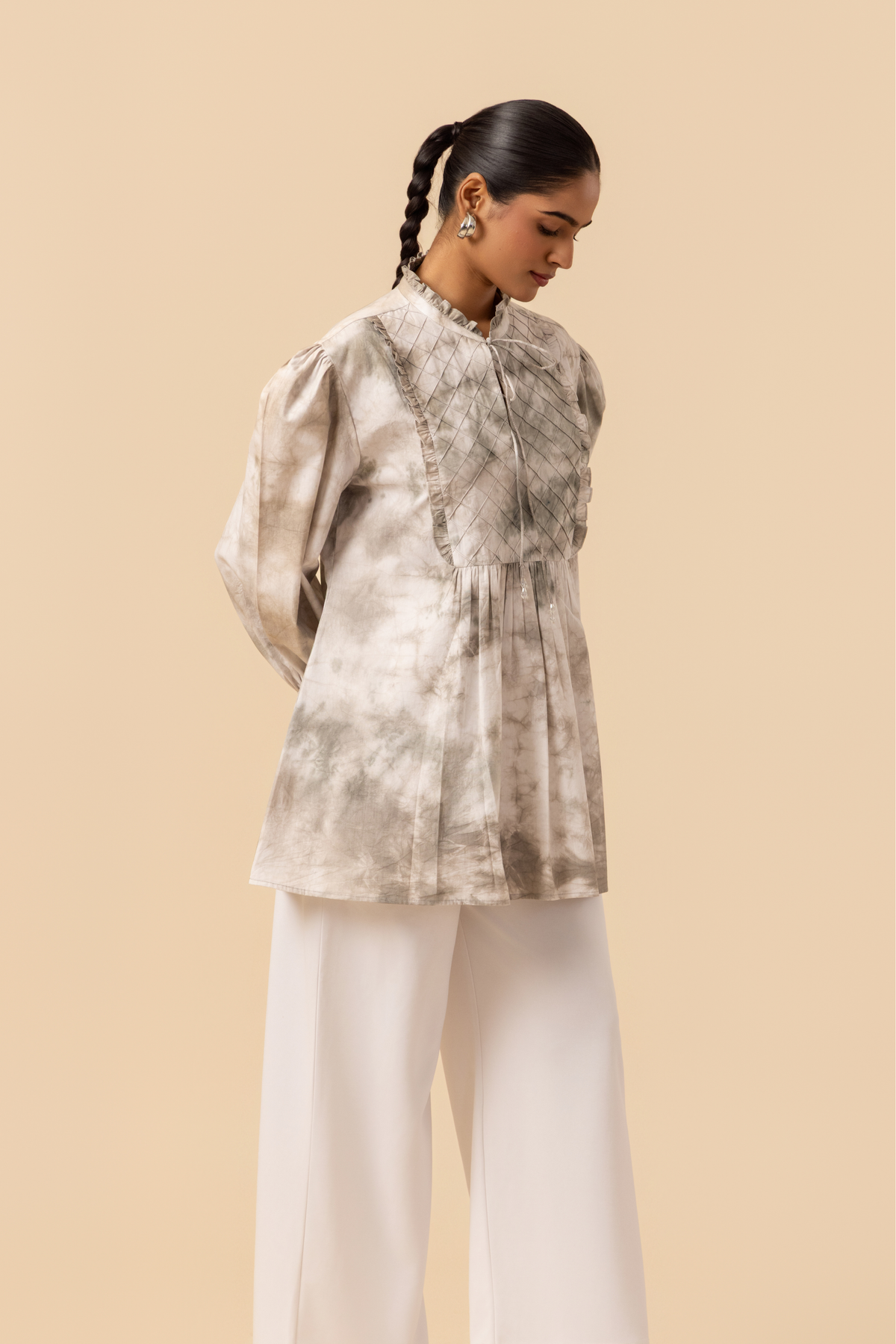 Right side view of a model wears a vibrant white & grey tie-dye shirt dress with puffed sleeves, paired with white wide-leg trousers and stylish sandals.