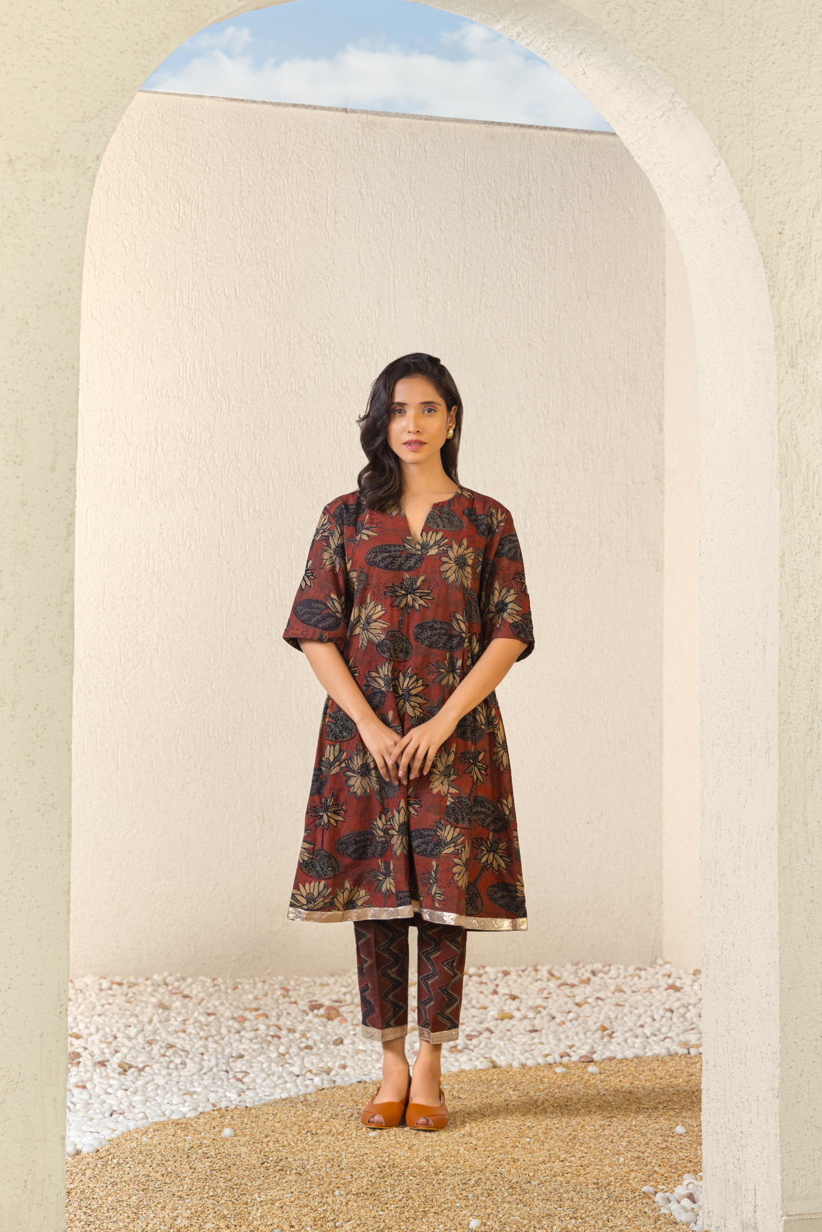Model showcasing a maroon floral linen kurta set with coordinated pants, styled against a serene outdoor archway backdrop