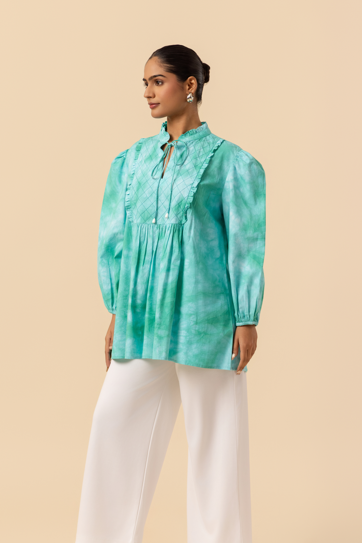 Side view of a model wears a vibrant ocean mist tie-dye shirt dress with puffed sleeves, paired with white wide-leg trousers and stylish sandals.