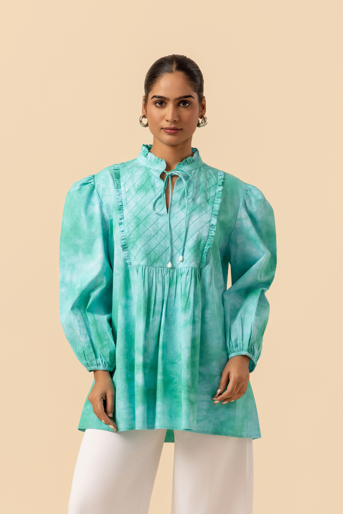 Closeup view of a model wears a vibrant ocean mist tie-dye shirt dress with puffed sleeves, paired with white wide-leg trousers and stylish sandals.