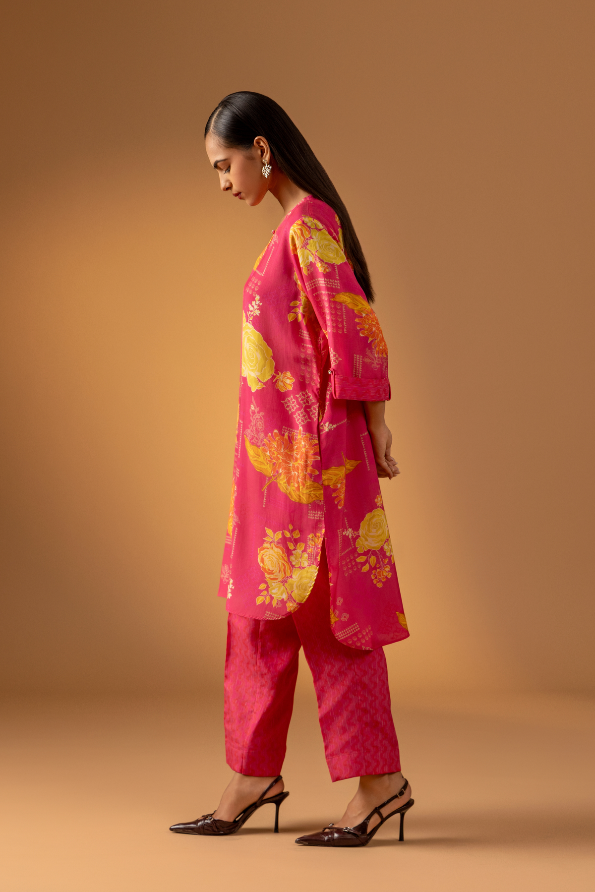 Side view of a model showcases a vibrant pink floral co-ord set with matching pants, set against a warm neutral background.