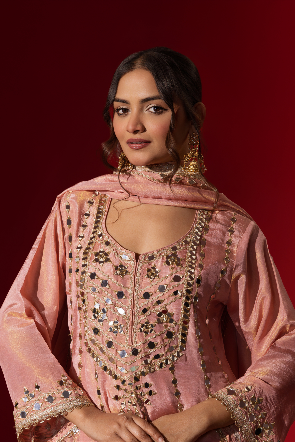 Closeup view of a woman stands elegantly in a rose embroidered kurta set with intricate patterns, complemented by a matching dupatta against a bold red background.