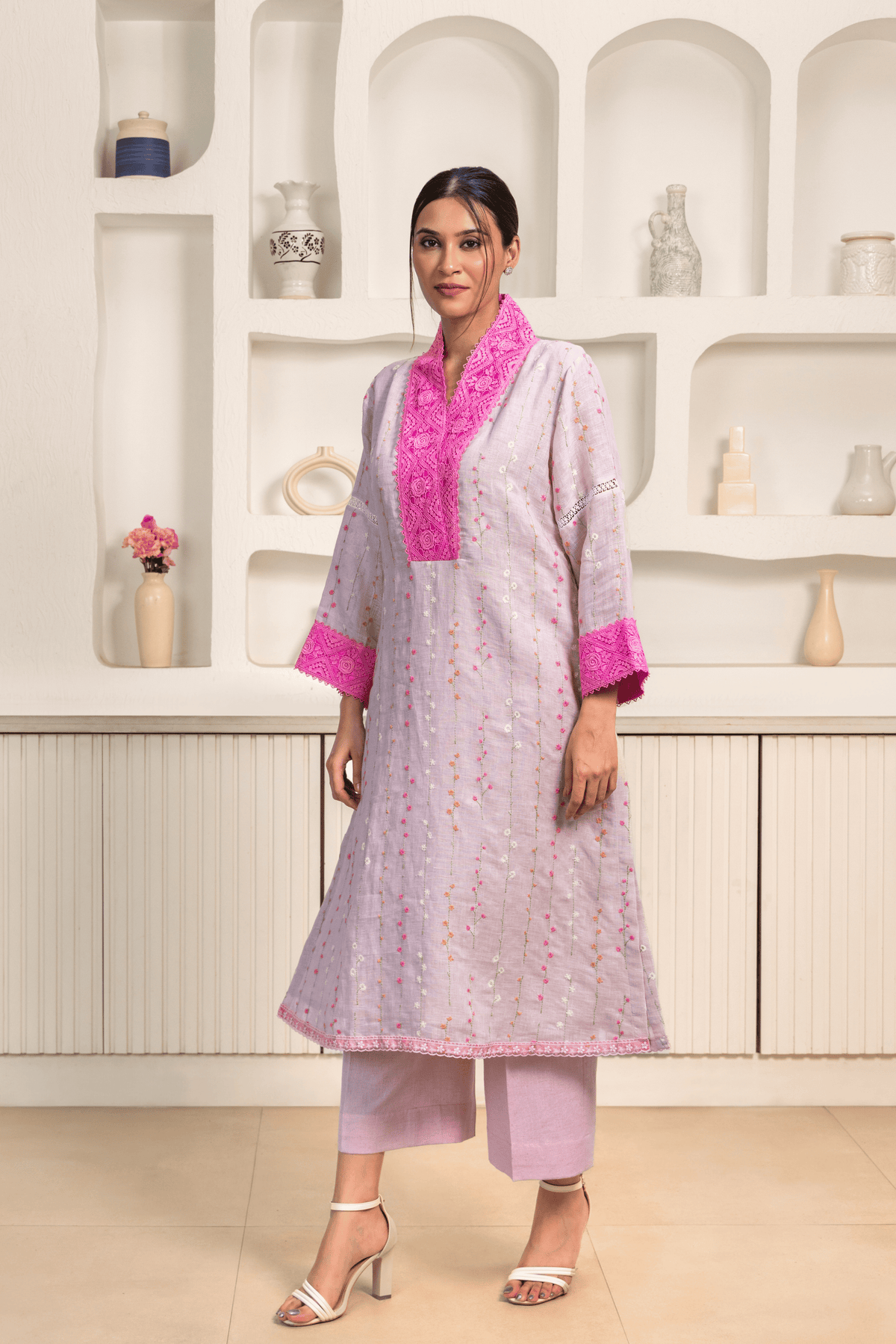 A model is dressed in a light lavender kurta adorned with vertical embroidery patterns and bright pink lace detailing on the collar and cuffs.