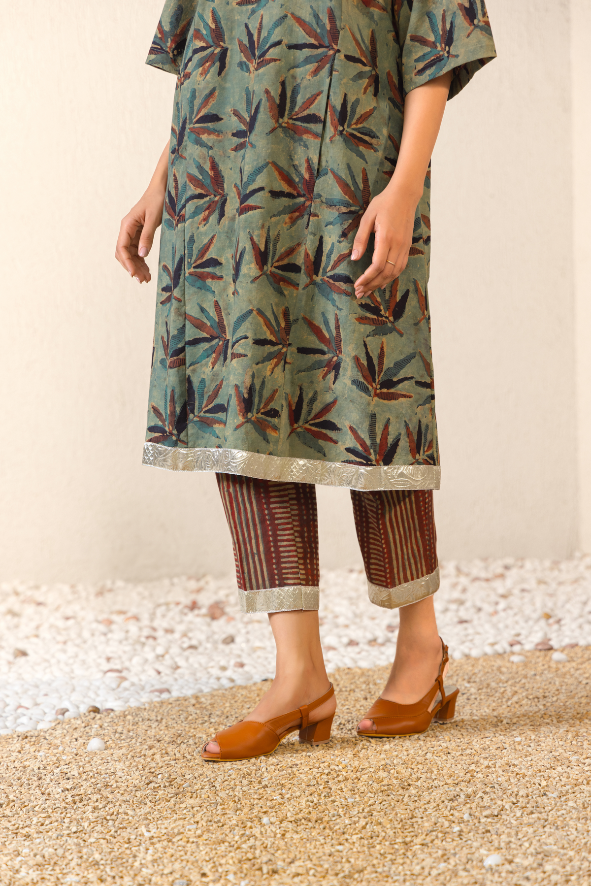 A close-up of a woman wearing a green printed kurta with matching pants, paired with brown heeled sandals.