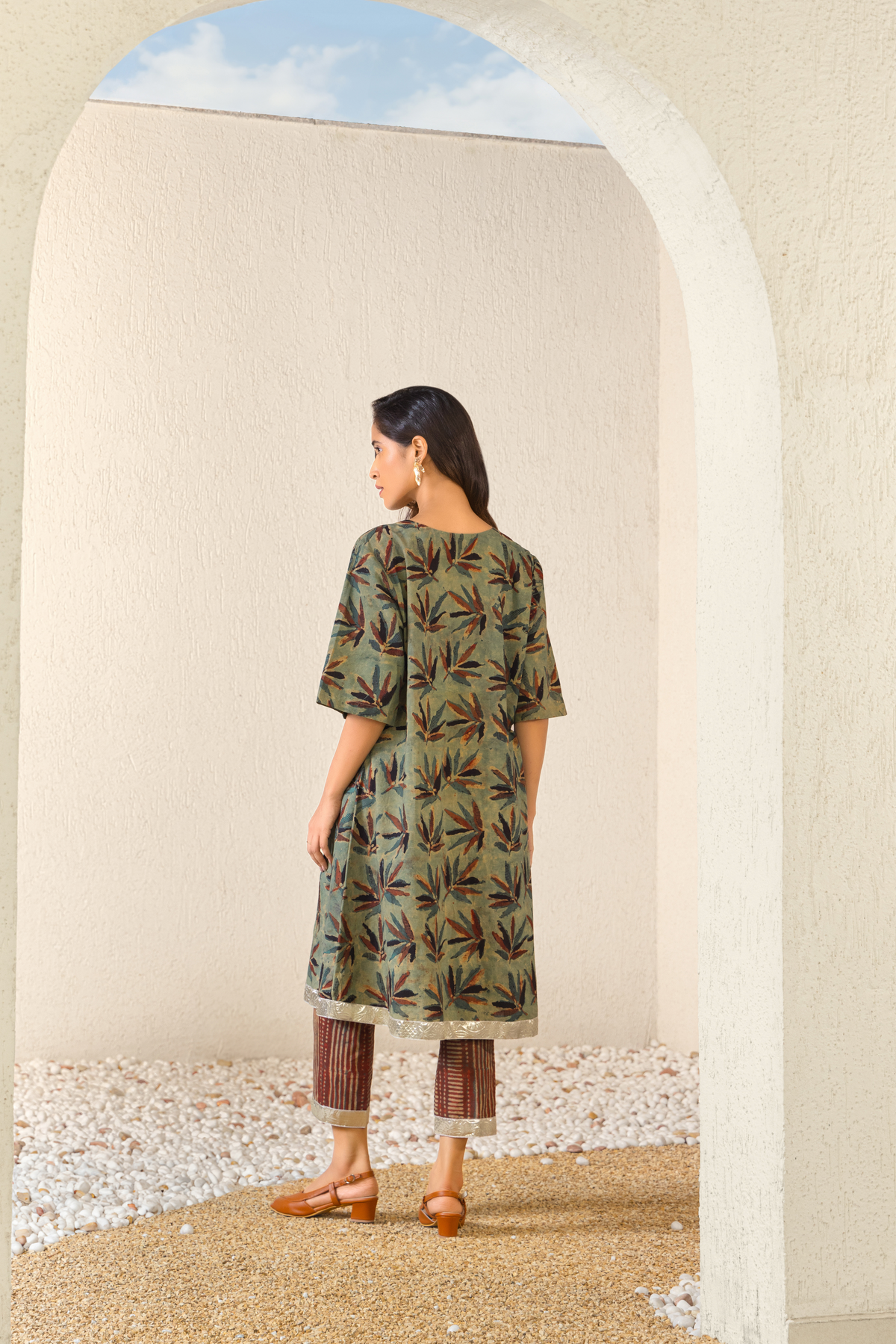 Back View of a woman wearing a green botanical print linen kurta set with matching pants, styled in a minimalist outdoor archway setting.