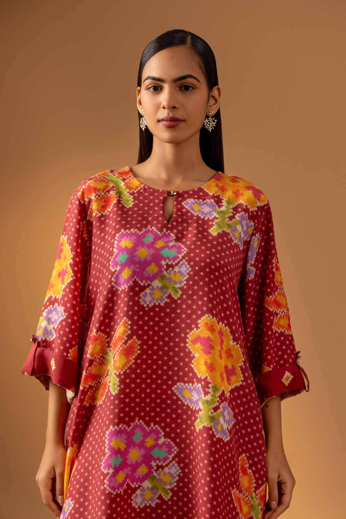 Closeup view of a model wears a vibrant floral co-ord set over matching patterned pants, set against a warm, neutral backdrop.