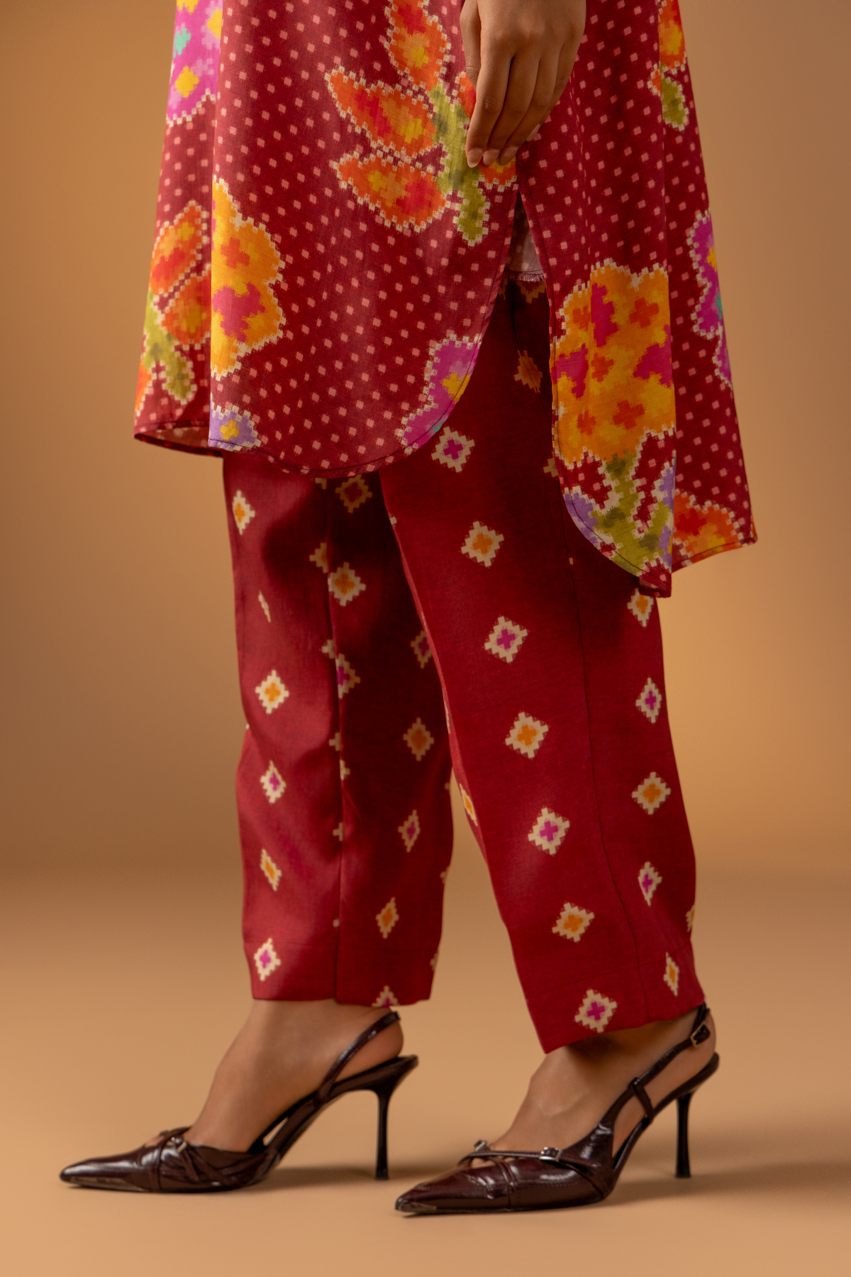 Closeup view of a woman wears a vibrant floral co-ord set over matching patterned pants, against a warm, neutral backdrop.