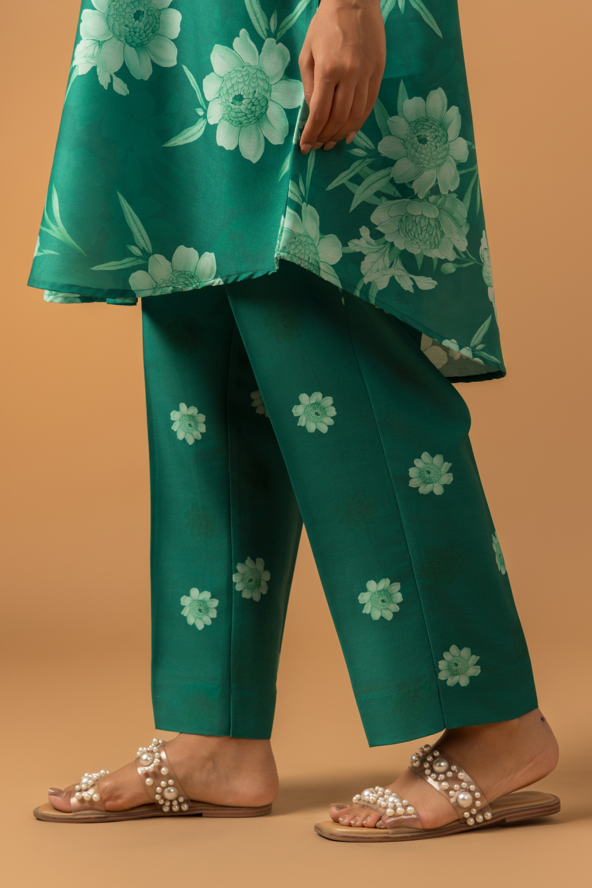 Close-up view of a woman wearing in a vibrant green floral co-ord set, featuring a loose shirt and matching pants, complemented by embellished sandals.