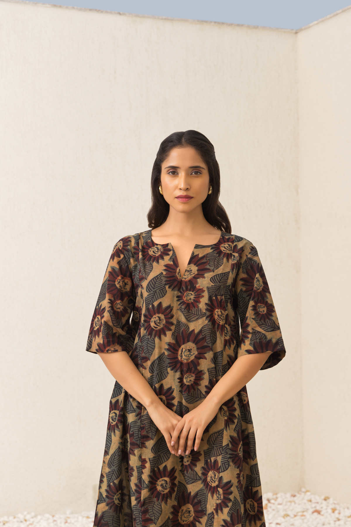 A person stands against a plain wall, wearing a ajrakh print co-ord set