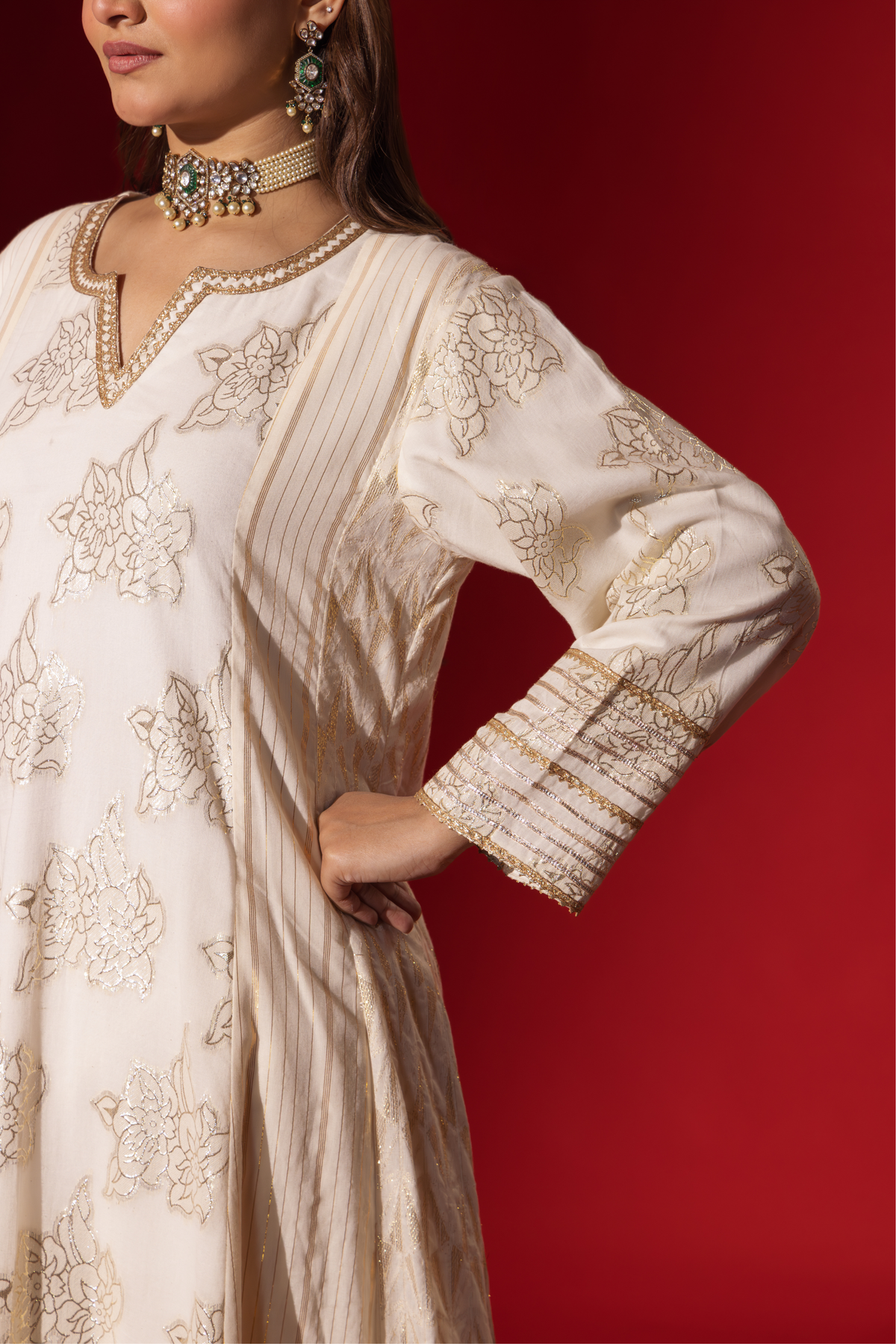 Closeup view of a woman's hand wearing an elegant white anarkali kurta set with intricate designs, contrasting beautifully against a deep red background.