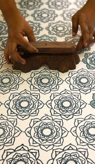 Hands using a wooden block to print intricate floral designs on fabric, showcasing traditional textile art.