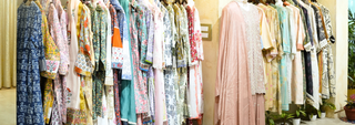 Colorful women’s ethnic dresses and kurtas hanging on a clothing rack in a boutique, featuring floral prints, pastel shades, and embroidered details.
