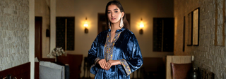 Woman wearing a navy blue velvet embroidered kurta with statement earrings, standing indoors in a softly lit, elegant setting.