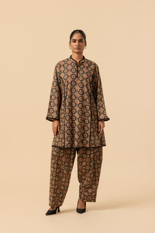 A woman modeling a two-piece traditional ajrakh co-ord set with a brown and black geometric pattern, consisting of a long-sleeve kurta and matching wide-leg pants, set against a solid beige background.