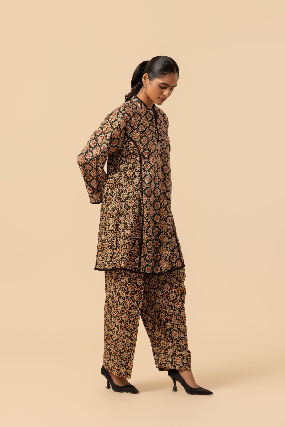 A woman modeling a brown and black patterned ajrakh co-ord set against a solid beige studio background.
