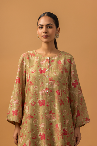 Closeup view of a woman in floral-patterned co-ord set with matching pants stands against a tan background, conveying a calm and elegant tone.