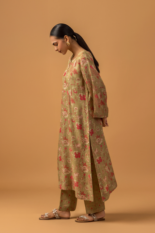 Side view of a woman in floral-patterned co-ord set with matching pants stands against a tan background, conveying a calm and elegant tone.