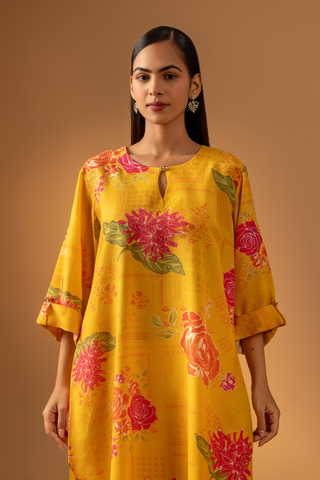 Closeup view of a woman in a vibrant yellow floral co-ord set and matching pants stands confidently against a warm, neutral background.
