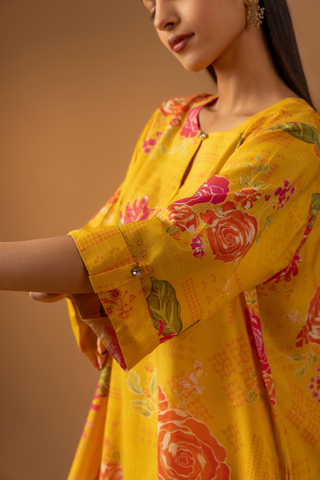 Closeup view of a woman showing her hand & wearing a vibrant yellow floral co-ord set and matching pants stands confidently against a warm, neutral background.