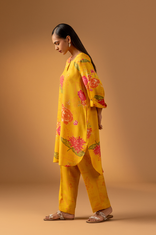 Side view of a woman in a vibrant yellow floral co-ord set and matching pants stands confidently against a warm, neutral background.