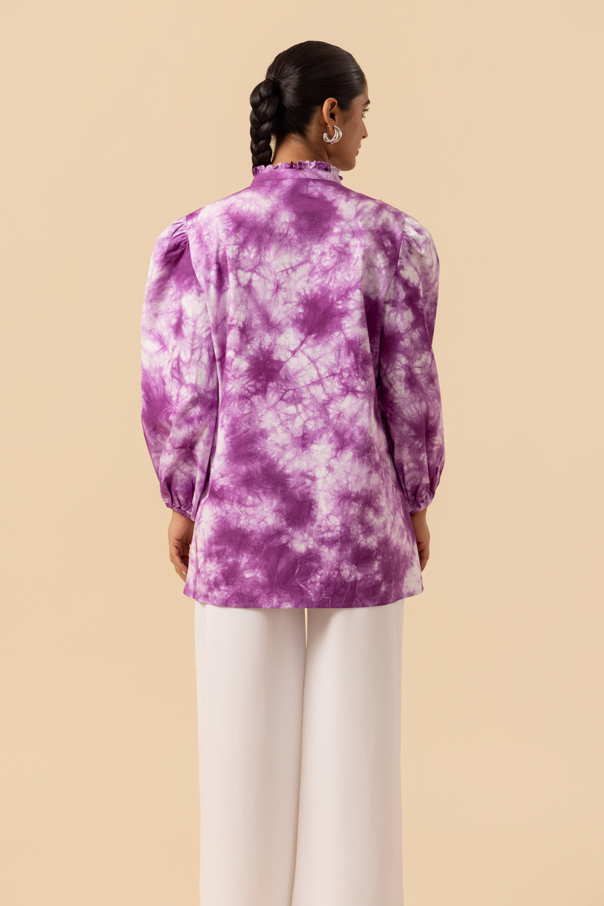 Back side view of a model wears a vibrant purple tie-dye shirt dress with puffed sleeves, paired with white wide-leg trousers and stylish sandals.