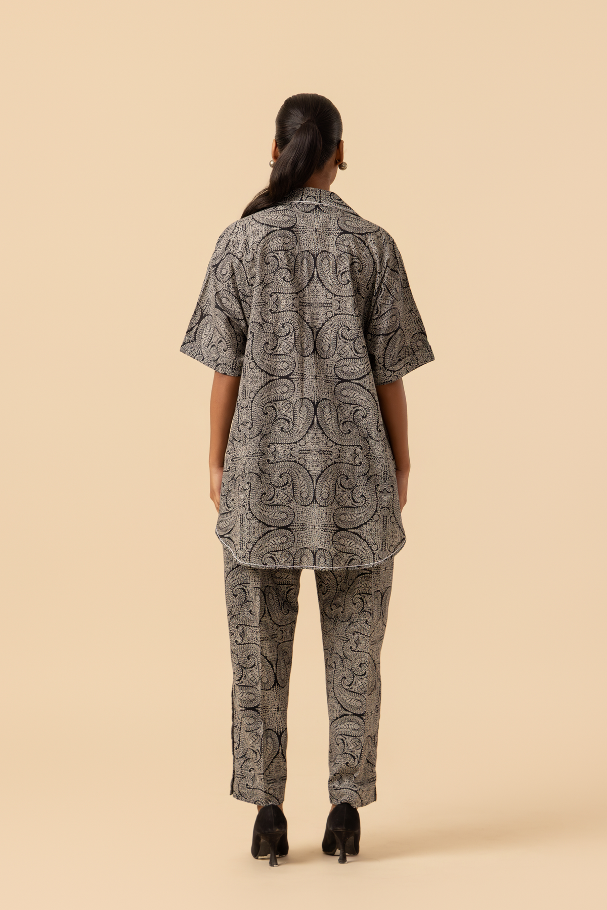 Back view of a person stands confidently in a matching patterned outfit, featuring a loose shirt and tailored pants, paired with stylish heels.