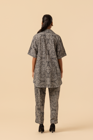 Back view of a person stands confidently in a matching patterned outfit, featuring a loose shirt and tailored pants, paired with stylish heels.