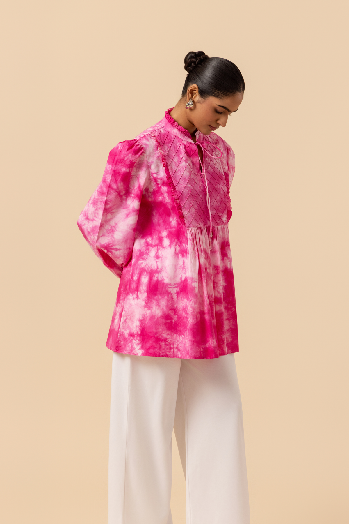 Right side view of a model wears a vibrant pink tie-dye shirt dress with puffed sleeves, paired with white wide-leg trousers and stylish sandals.