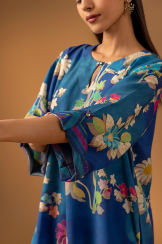 Closeup view of a woman showing her hand & wearing a vibrant floral co-ord set paired with striped pants, set against a warm, neutral background.