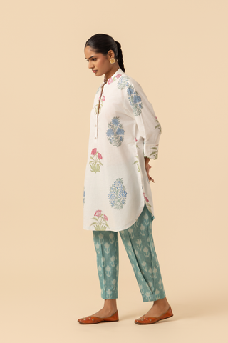Side view of a woman stands wearing a floral-printed tunic and teal pants cotton co-ord set, set against a soft beige background, showcasing a stylish ethnic outfit.