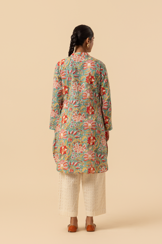 Back view of a person stands elegantly in a colorful floral co-ord set paired with white embellished pants and traditional sandals against a soft beige background.
