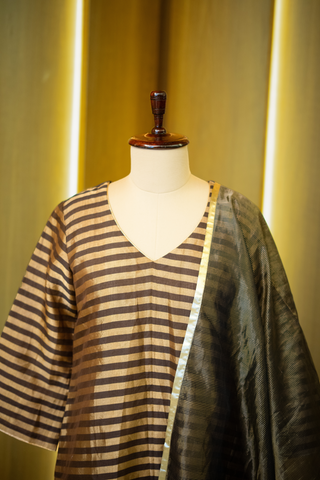 closeup view of black and gold striped kurta paired with a sheer, shimmering dupatta, displayed on a mannequin against a warm wooden backdrop.