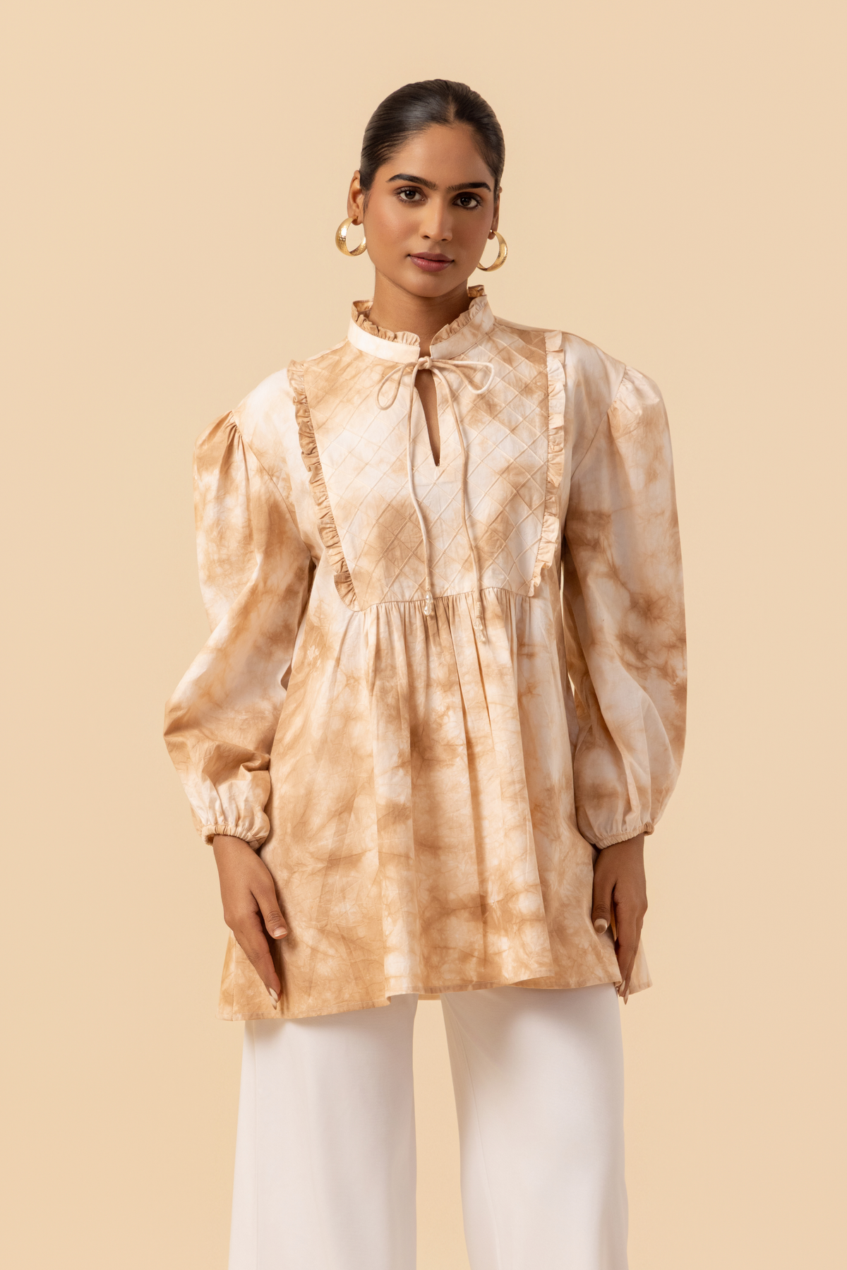 Closeup view of a woman wears a vibrant caramel tie-dye shirt dress with puffed sleeves, paired with white wide-leg trousers and stylish sandals.