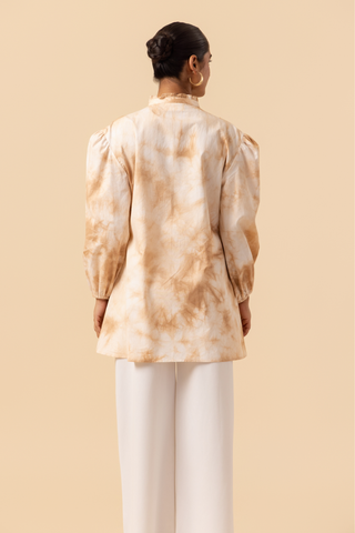 Back view of a woman wears a vibrant caramel tie-dye shirt dress with puffed sleeves, paired with white wide-leg trousers and stylish sandals.